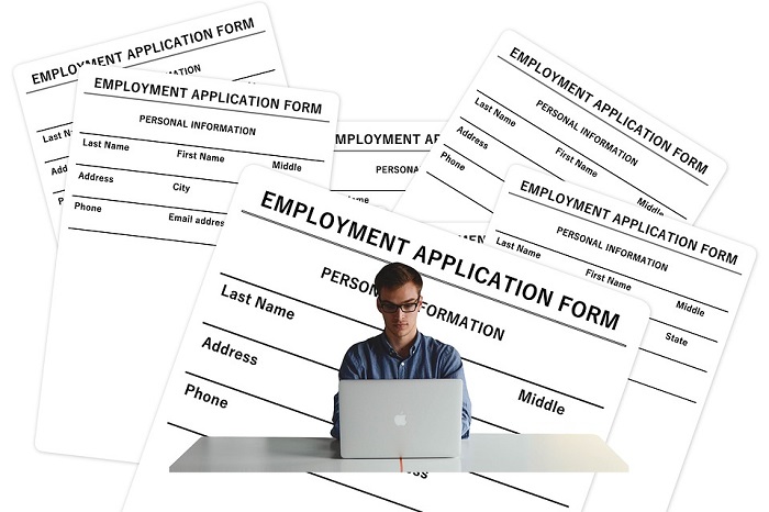 Man at a desk with a computer in front and piles of unfilled Employment Application Forms behind him